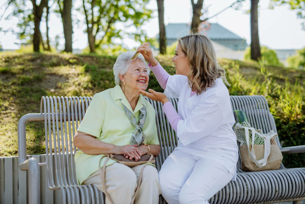 Dominion of Anderson | Senior woman sitting on a bench with her caregiver, and getting her hair combed