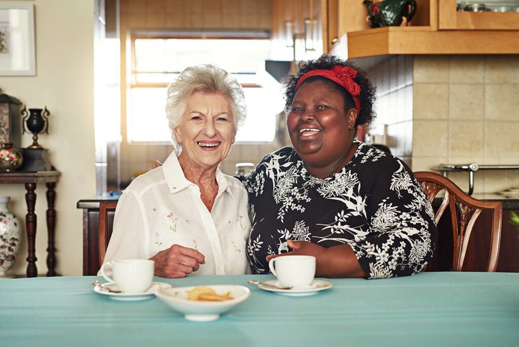 Dominion of Louisville | Senior woman and her caregiver sitting at a table having coffee